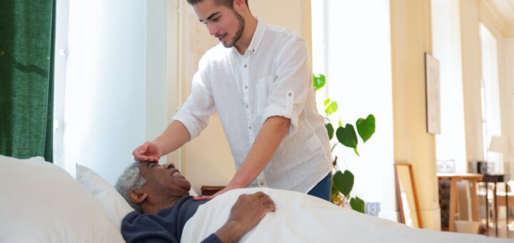 An image of hospice care where a younger man comforts and older adult lying in bed
