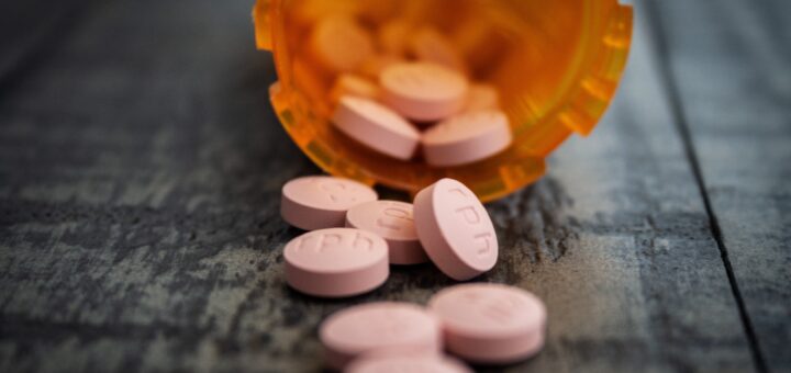 An orange prescription bottle tipped over on a black surface with light orange pills spilling out