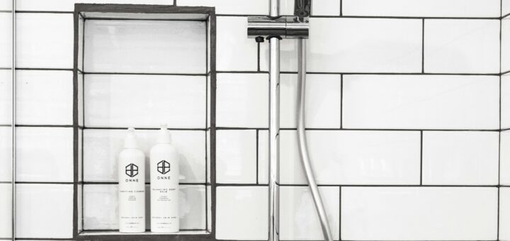 Shower with white subway tile and chrome and black fixtures. Two bottles of shampoo or conditioner are on built in shelf