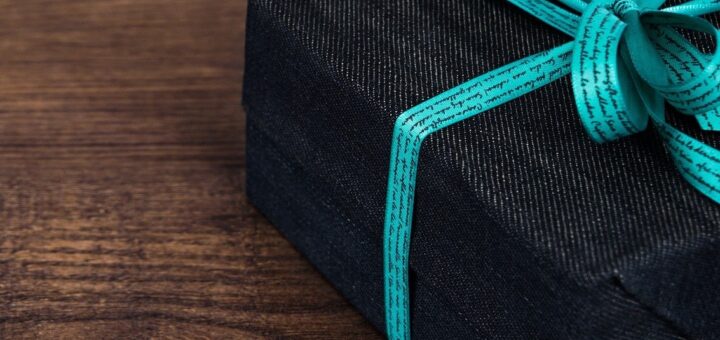 The background is a brown wood table. In the foreground and off to the side is a package wrapped in handsome dark brown paper tied up in teal ribbon with a nice bow