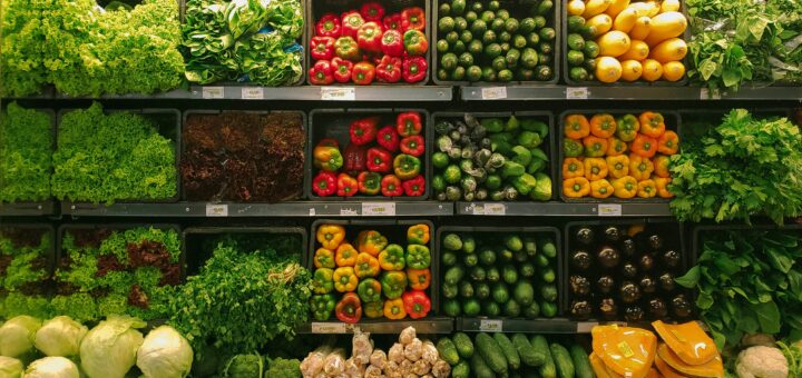 A produce aisle full of brightly colored vegetables like red and green peppers, green lettuce, yellow onions
