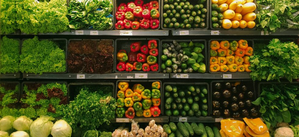A produce aisle full of brightly colored vegetables like red and green peppers, green lettuce, yellow onions
