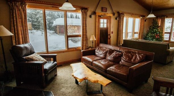 Image of a large room interior with multiple windows and seating. Muted earth tones dominate, with a deep brown couch.