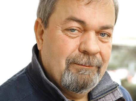 Closeup of a man's face. He has thinning brown hair mixed with gray and a graying beard and mustashe. He's looking at the camera with challenging eyes, seeming to question your reaction.