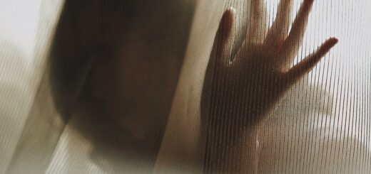 Image shows a female silhouette peering between window sheers.. Her hand is on the glass and she looks like she's wishing for help