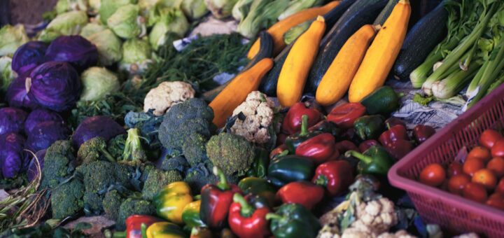 A colorful array of vegitables in a store showing carrots, red peppers, green peppers. broccoli, cauliflower, and more.