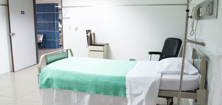 This image shows a classic hospital room with a insturtional cover over sheets on a hospital bed. There's is a gray visitor's chair near the bed.