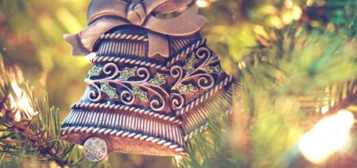 The background image shows blurred fall trees. In the foreground, there are two brown needlework -appearing bells tied with beige velvet-type ribbon.