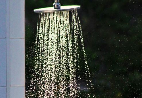 The image is of a running showerhead viewd from the side before entering. The shower surround is blurred and dark.
