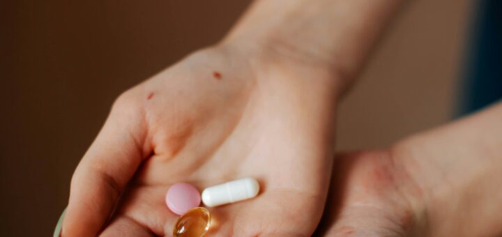 This indoor image shows two cupped hands containg small pills. One is a white capsule, one is a small round orange tablet.