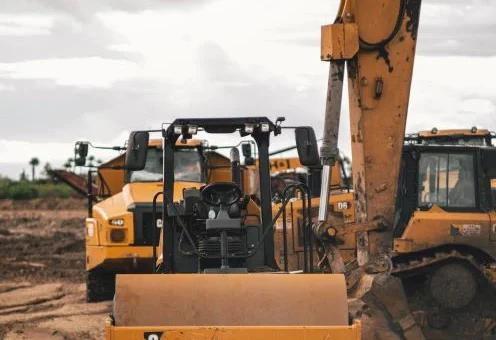 This image shows a cloudy, gray day on a construction site. We see a massive, classic yeallow digger from the rear with the bucket raised.