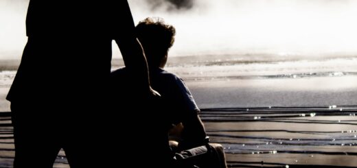 This black and white image shows a cloudy evening view as an older man pushes an older woman in a wheelchair. They image can be interpreted as lonely or peaceful, depending on the viewer.