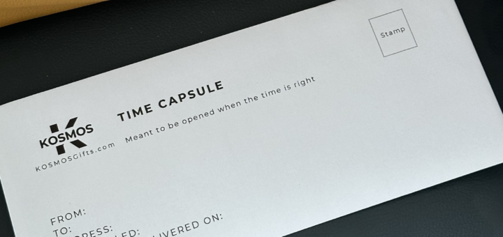The image shows an envelope resting on a black mat on top of a brown table or desk. The envelop shows a KOSMOS logo and the words Time Capsule. In addition, the viewer sees instructions for the person using the envelope.