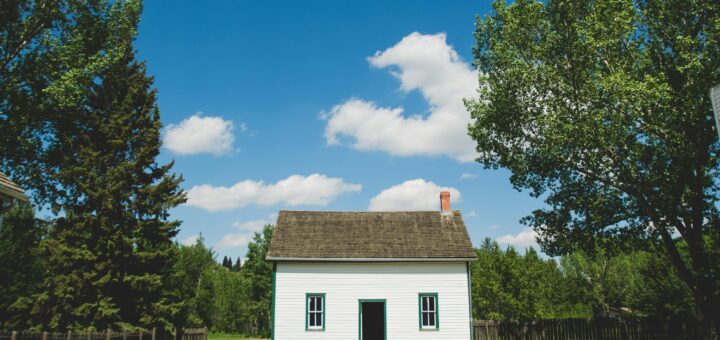 A small cottage-like home with white siding is set back in a yard with trees.
