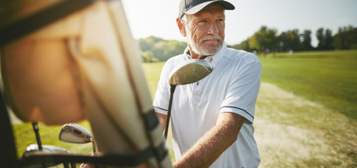 A middle-aged man wearing a white golf shirt stands holding a club as he determines his next swing.