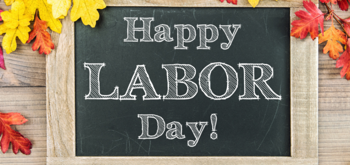 The background shows a weathered board with fall leaves draped across the top. Centered, is a chalkboard o which Happy Labor Day has been printed in block letters.