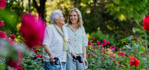 A younger woman strolls in a garden with an older woman who uses a rollator. They are enjoying each other's company.