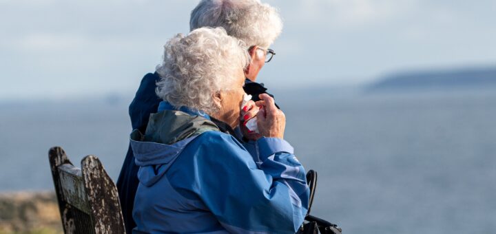 An older couple sites side by side on a bench, looking out over a lake.