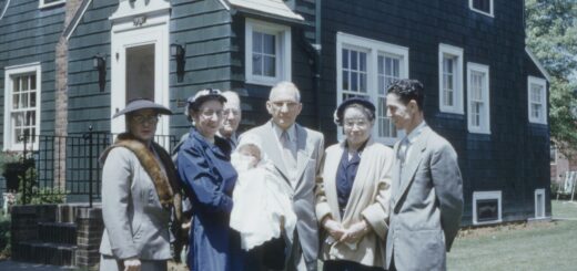 A vintage, faded color photo shows a group of older adults standing together, enjoying having their picture taken.