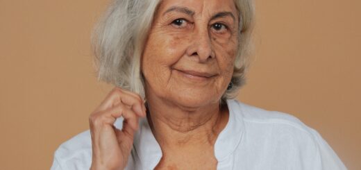 An older woman with white hair cut in a stylish bob and wearing a white pullover shirt with a v neck looks out at the camera. She's tugging a bit on one side of her hair.