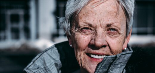 An older woman with short gray hair smiles toward the camera. She appears vital and alive as she peers around the standup collar of her fall coat.